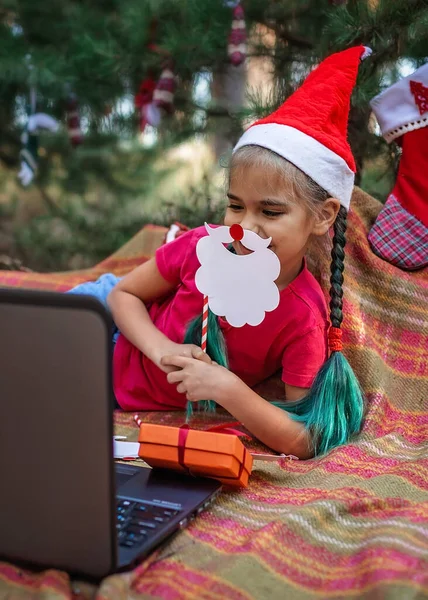 New normal online Christmas celebration. Cute sibling using laptop and festive fun props to celebrate Christmas with family via video chat, happy holidays, outdoor