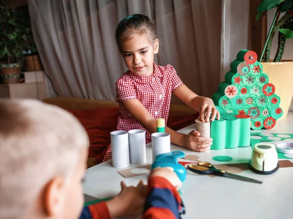 Cute little kid making handmade advent calendar with toilet paper rolls at home. Glue, colored paper, cut punch to hide sweets and candies in rolls. Seasonal activity for kids, family winter holidays — Stock Image Cute Little Kid Making Handmade Advent Calendar Toilet Paper Rolls Royalty Free Stock Photos