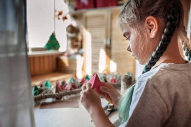 Sevimli küçük çocuk renkli kağıt üçgenli el yapımı takvim yapıyor. Şekerler ve şekerler dalda asılı renkli üçgenlerde saklıdır. Çocuklar için mevsimlik etkinlik, aile kış tatili