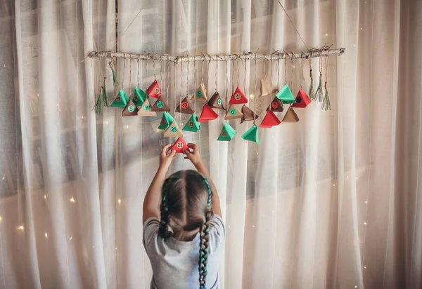 可爱的小孩打开手工制作的带有彩纸三角形的日历 糖果和糖果藏在挂在树枝上的五彩缤纷的三角形里 儿童季节性活动 家庭寒假 — 图库照片