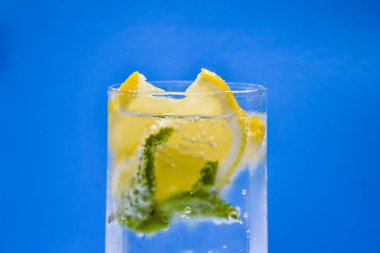 Mineral su limon ve nane yaprakları mavi arka plan üzerinde infüzyon.
