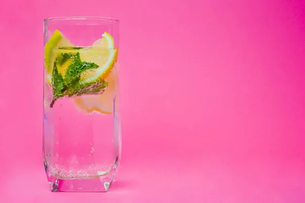 Su, limon ve nane pembe bir arka plan üzerinde.