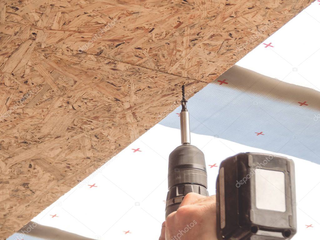 Builder twists the screw in the OSB sheet on the ceiling