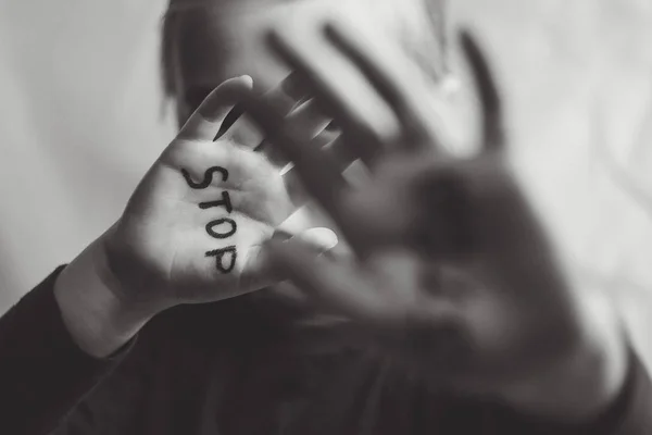 Little frightened girl shows the word "Stop" written on the arm. Children are subjected to violence and publishing in the home and school concept and the rights of children. Black and white photo. — Stock Photo, Image