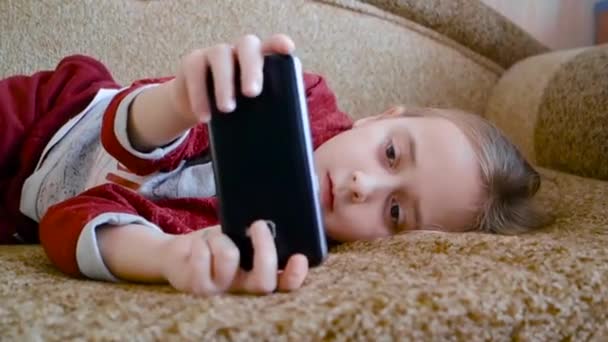 Teenager-Mädchen spielt im Telefon, während sie auf der Couch liegt. — Stockvideo