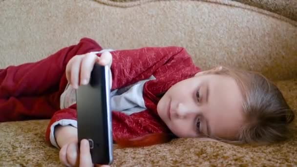Adolescente chica jugando en el teléfono mientras está acostado en el sofá . — Vídeo de stock