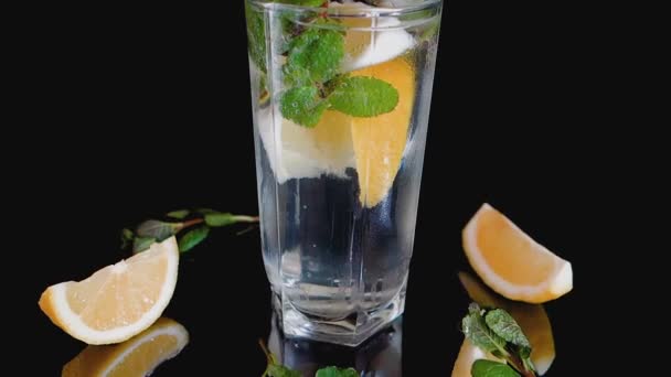 Sparkling cocktail with slices of lemon, ice cubes and mint on a dark background. — Stock Video