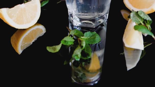 Sparkling cocktail with slices of lemon, ice cubes and mint on a dark background. — Stock Video