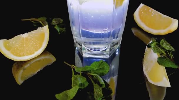 Sparkling cocktail with slices of lemon, ice cubes and mint on a dark background — Stock Video