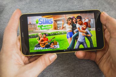 Berdyansk, Ukraine - March 4, 2019 - Close up of hand of person playing The Sims Mobile game apllication. clipart