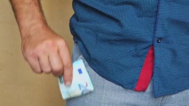 Bir adam pantolon cebine euro banknotlar koyar. Bir adam cebinde para saklar..