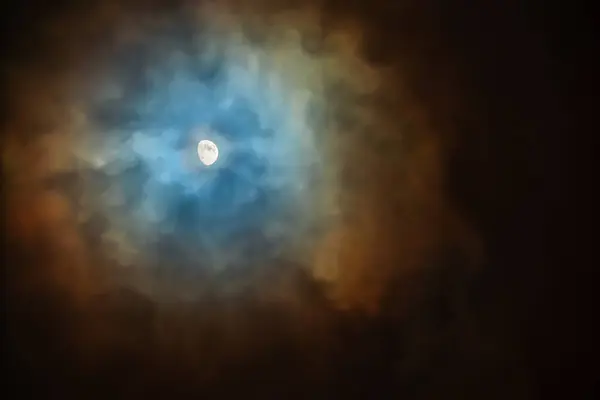 The Moon in the sky on a cloudy night is surrounded by colored clouds. Corona - in meteorology plural coronae is an optical phenomenon produced by the diffraction of moonlight by water droplets or tiny ice crystals of a cloud