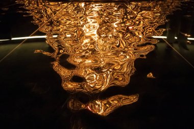 Soyut bir ateş ışığı deseni ve parlak bir yüzeyde yansımalar, altın kıvrımlar ve parıltılarla. Şekilsiz bir yapının zıt görünümüne sahip doğal ve garip bir arka plan.