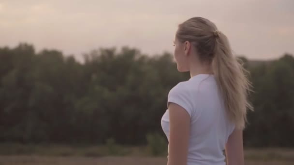 A girl in a white t-shirt in the rays of the setting sun performs breathing exercises. Against the forest and sunset. The athlete during the holidays. Active rest and beautiful landscape.