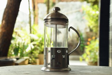 Fransız Basını olarak adlandırılan kahve yapmak için kullanılan bir araç, bir kafenin doğal arka planına sahip ahşap bir masanın üzerindedir..