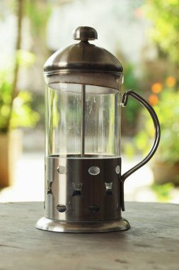 Fransız Basını olarak adlandırılan kahve yapmak için kullanılan bir araç, bir kafenin doğal arka planına sahip ahşap bir masanın üzerindedir..