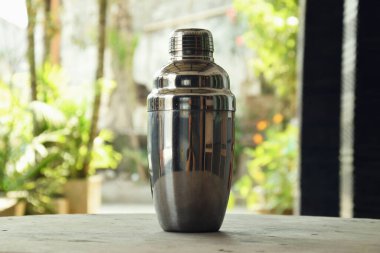 Bir kafenin doğal arka planına sahip ahşap bir masada, sıklıkla Kokteyl Sallayıcısı olarak adlandırılan içki yapmak için bir araç kapatın.