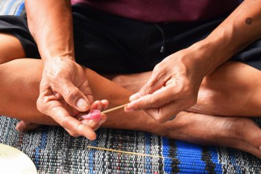 The hands of a middle-aged Indonesian man are skewering goat meat with a bamboo skewer to be made into grilled satay during the Eid al-Adha celebrations.