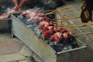 Some raw goat meat is skewered using bamboo and grilled on a charcoal grill. This is the process of making Indonesian goat satay during the Eid al-Adha celebration.