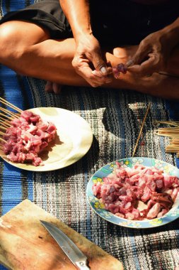 Close-up of a man's hand skewering goat satay with a bamboo skewer. The process of making satay during Eid al-Adha in Indonesia.