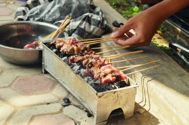 A person flips a piece of goat satay being grilled over charcoal. The process of making satay during Eid al-Adha in Indonesia.