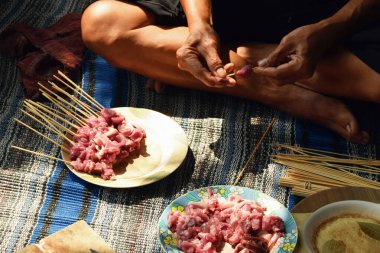 Close-up of a man's hand skewering goat satay with a bamboo skewer. The process of making satay during Eid al-Adha in Indonesia.