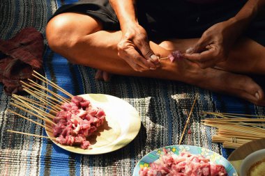 Close-up of a man's hand skewering goat satay with a bamboo skewer. The process of making satay during Eid al-Adha in Indonesia.