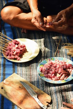 Close-up of a man's hand skewering goat satay with a bamboo skewer. The process of making satay during Eid al-Adha in Indonesia.