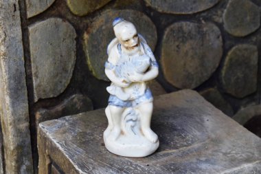 A small statue of an Asian old man carrying a big fish in his arms with rocks. The art of a small statue is a symbol of prosperity.