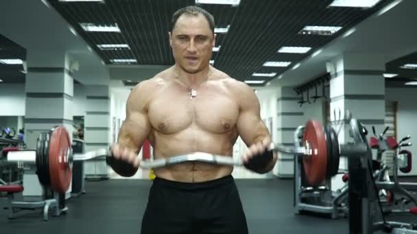 Sportsmanen fungerar med händerna i gymmet. Han lyfter barbell och fungerar på biceps. — Stockvideo