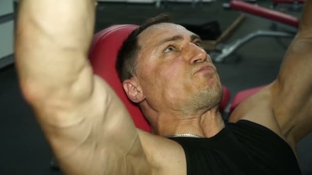 Ισχυρός άνδρας σηκώνει βάρη πάνω από το κεφάλι στο γυμναστήριο. — Αρχείο Βίντεο