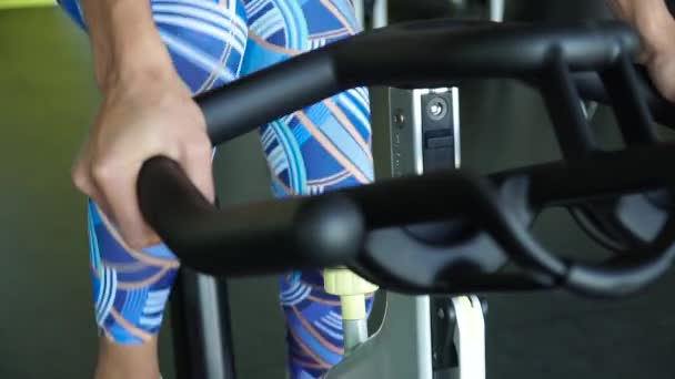 Motionscykel - en kvinna utövar på en stillastående cykel i ett gym — Stockvideo