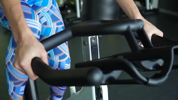Motionscykel - en kvinna utövar på en stillastående cykel i ett gym — Stockvideo