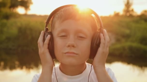 Jongen luisteren naar muziek via koptelefoons in de natuur onder de zonsondergang — Stockvideo