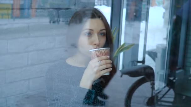 Una chica en un café bebe chocolate caliente de una taza de papel — Vídeos de Stock