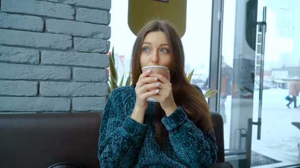 Una chica en un café bebe chocolate caliente de una taza de papel — Vídeos de Stock