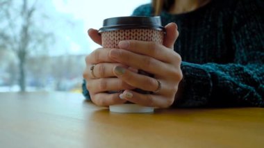 Bir kızın elinde sıcak bir cappuccino ile bir kağıt bardak.