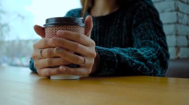 Bir kızın elinde sıcak bir cappuccino ile bir kağıt bardak.