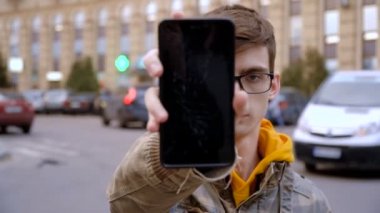 Kırık bir gadget kavramı. Sinirli genç adam kırık bir ekran ile bir smartphone gösterir.