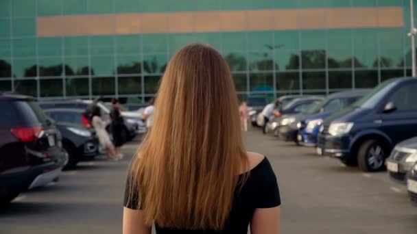 Kamera podąża za młodą atrakcyjną brunetką na parkingu. — Wideo stockowe