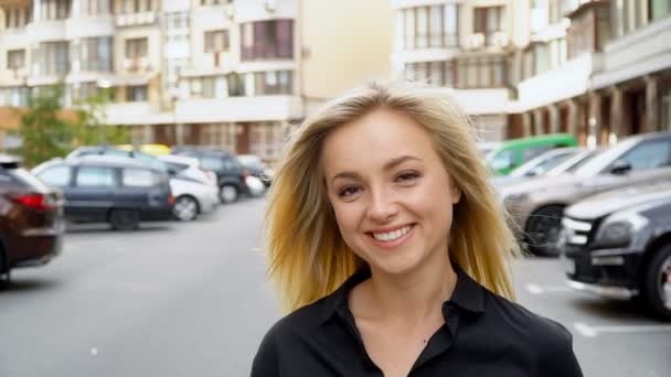 Portrét šťastné blondýny v černé košili na parkovišti — Stock video