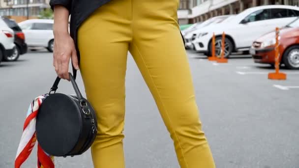 Блондинка в жёлтых брюках и в чёрной шляпе позирует на парковке. Проводка камеры снизу вверх — стоковое видео