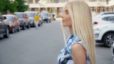 Otoparkta poz veren yazlık takım elbiseli bir sarışın. Kamera kabloları. Kadınlar yürür