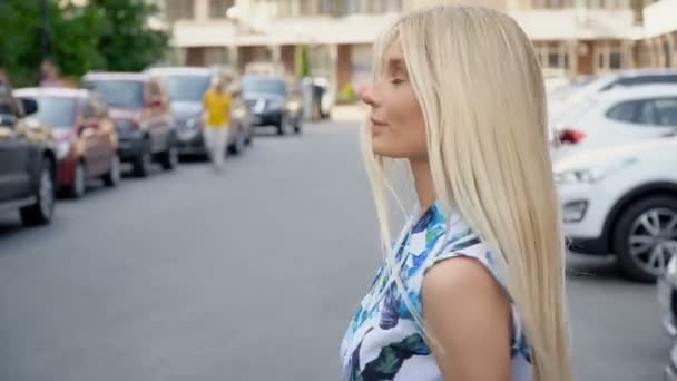 Otoparkta poz veren yazlık takım elbiseli bir sarışın. Kamera kabloları. Kadınlar yürür — Stok video