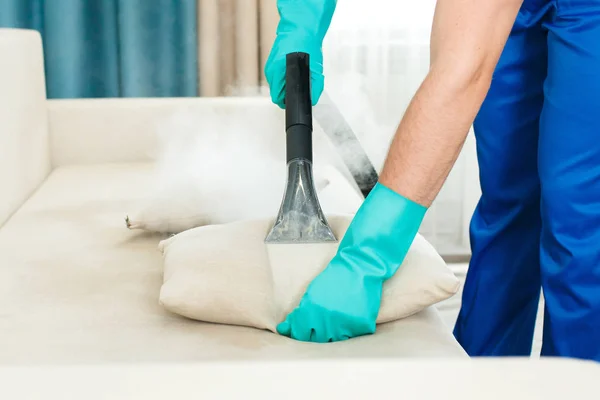 An employee of a cleaning company provides a chemical and steam cleaning service for the sofa. Steam cleaner