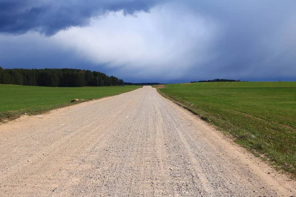 Kırsal, tarla, Avrupa'da çakıl yol, tüm yeşil bir alanın ortasında toz ile kaplı ve gökyüzünde fırtına kara bulutlar