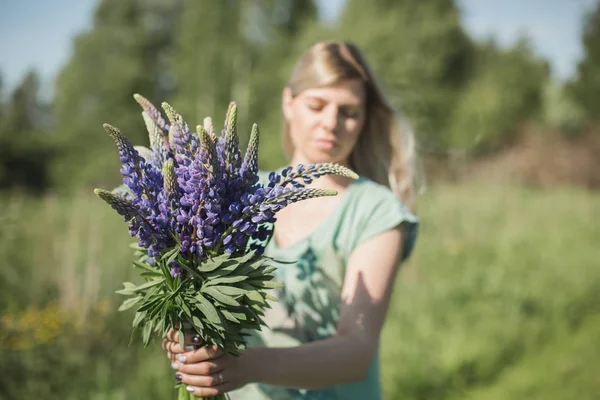 the girl is standing in the field with a bouquet of lupines