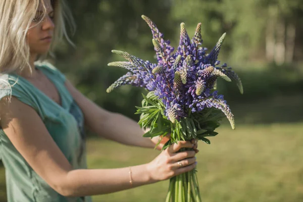 the girl is standing in the field with a bouquet of lupines