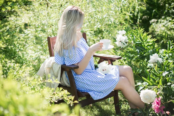 young woman is resting in the garden on a chair with a mug of tea