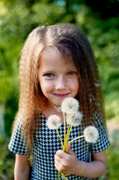 Baby 4 years, with blue eyes, small curls. A wonderful time of childhood and adventure. Warm sunlight.Holding a dandelion — Stock Photo, Image